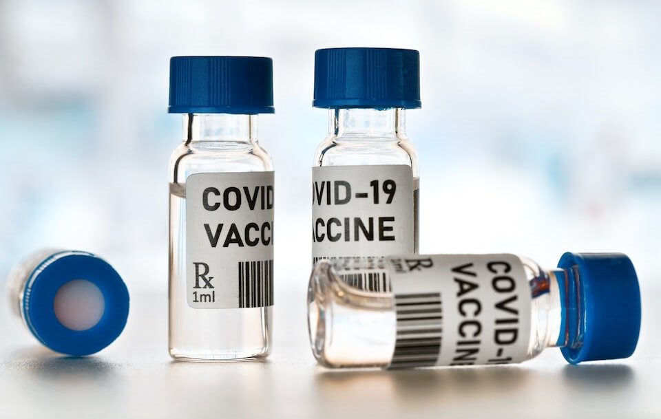 Three vials labeled "covid-19 vaccine" on a surface, with one vial lying on its side.