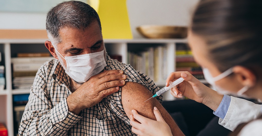 A healthcare worker administers a vaccine to an elderly man wearing a face mask.