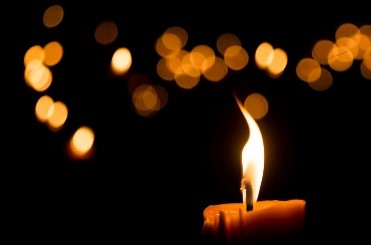 A lit candle with a blurred background of warm light bokeh.