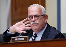 A man with glasses gestures while speaking at a committee hearing.