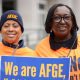 Two individuals wearing afge hats and orange shirts, one holding a sign that reads "we are afge.