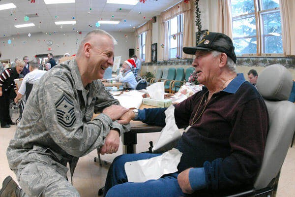 A military service member in uniform shares a laugh with an elderly individual at an indoor gathering.